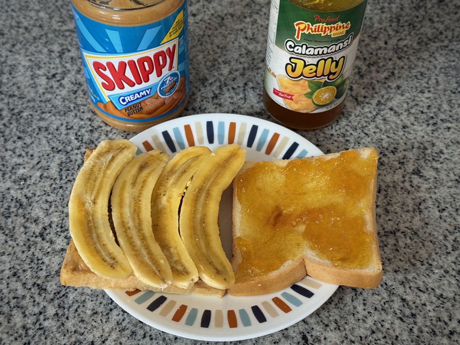 Open-faced toast with peanut butter, sliced bananas, and calamansi jelly on a plate, with the jars behind it on a kitchen counter.