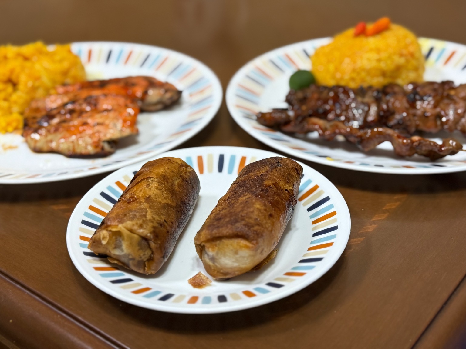 Two pieces of turon on a plate in the foreground, with skewers and bright yellow Java rice on plates behind them.