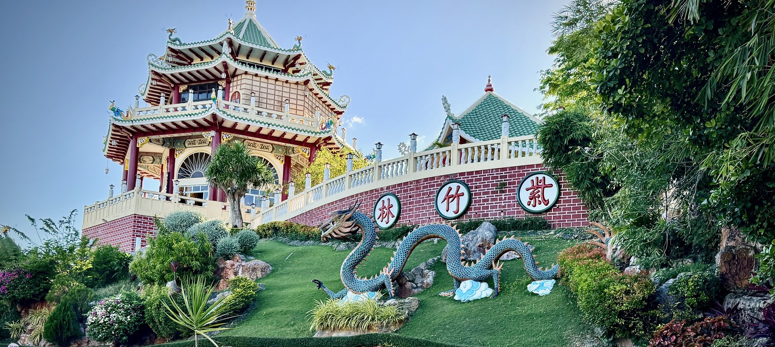 The Cebu Taoist Temple pagoda rising above a hillside garden, with a large blue dragon statue coiling across the green slope in the foreground.