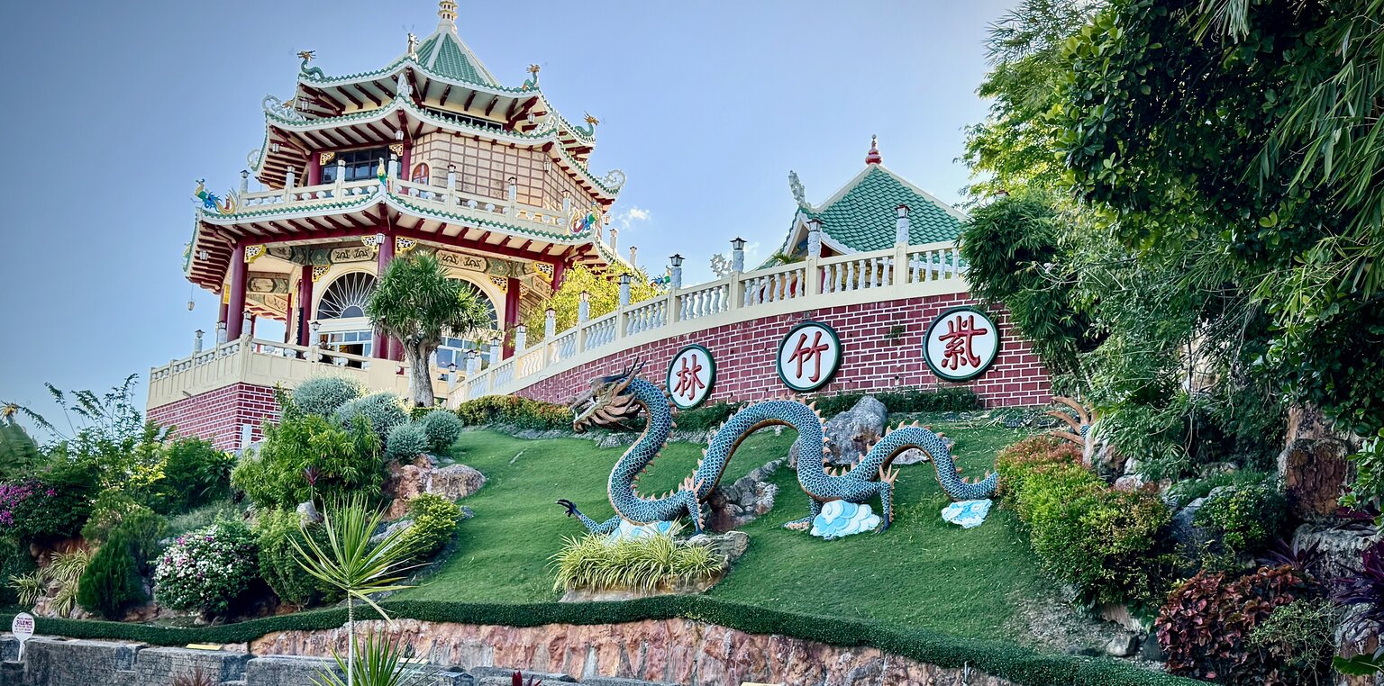 The Cebu Taoist Temple pagoda rising above a hillside garden, with a large blue dragon statue coiling across the green slope in the foreground.