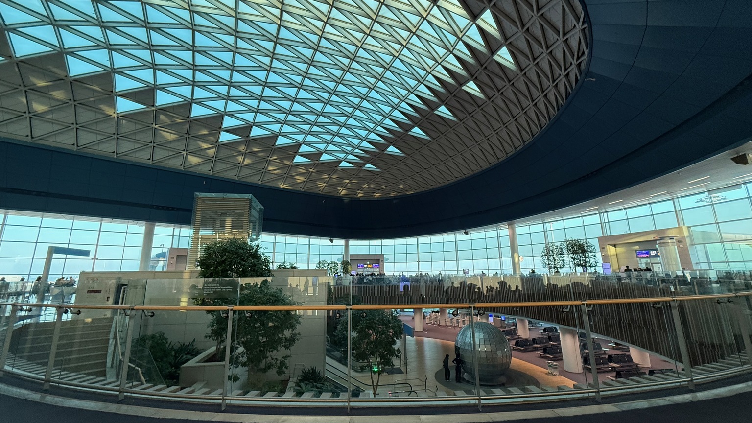 Wide view of the airport terminal with a curved glass roof and departure gates
