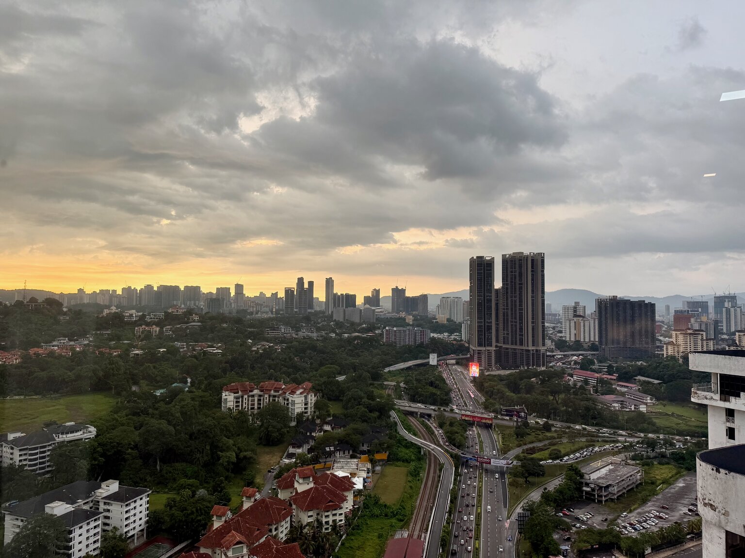 The Kuala Lumpur skyline at dusk under heavy clouds, viewed from a high-rise apartment window