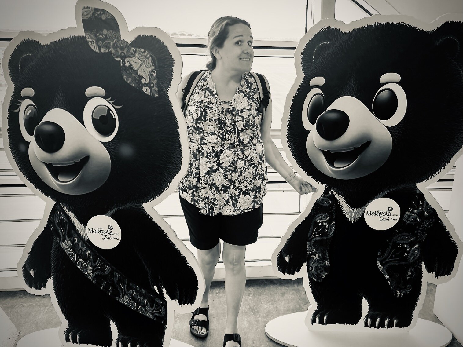 Marcia posed between two large golden bear mascots from Malaysia's Truly Asia 2026 tourism campaign at KL airport, both bears dressed in patterned outfits