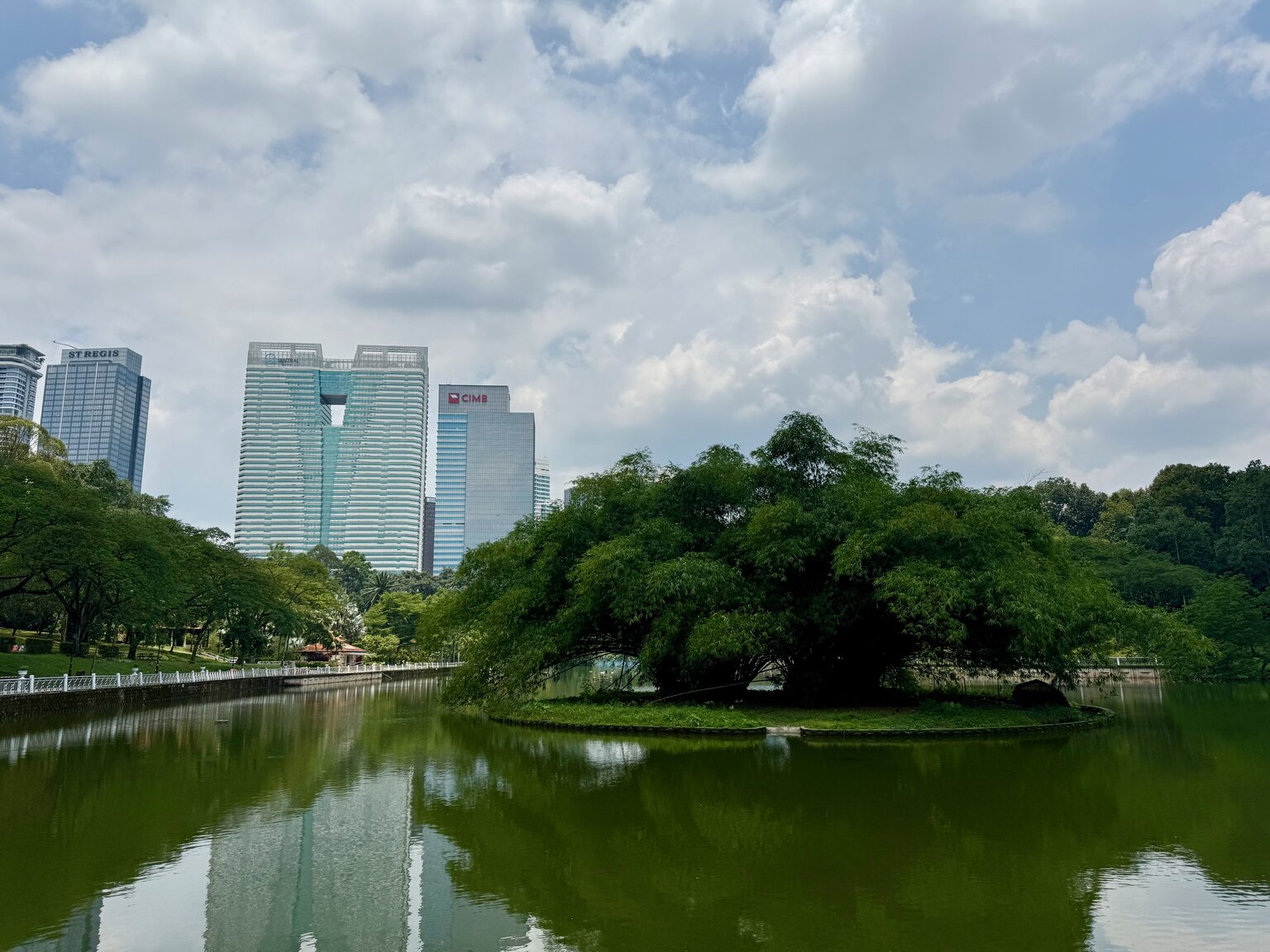 A small treed island on the lake at the Perdana Botanical Garden in Kuala Lumpur, with the city's high-rises visible through the trees in the background