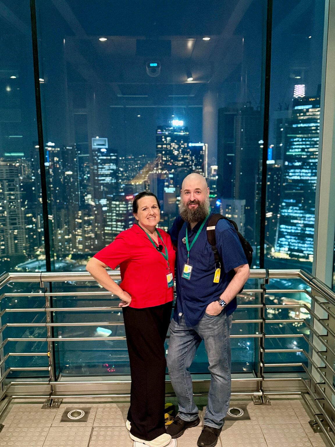 John and Marcia at a glass observation window high in the Petronas Towers, the lit Kuala Lumpur skyline behind them.