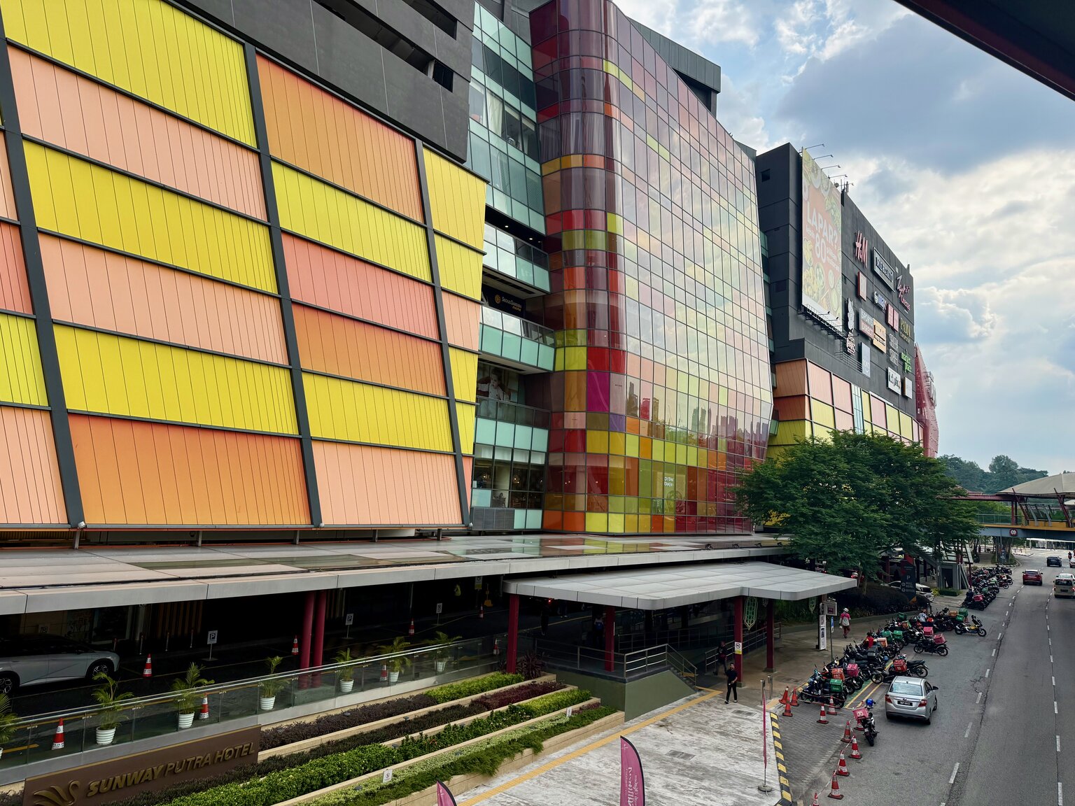 The colourful fused-glass façade of Sunway Putra Mall in Kuala Lumpur, with yellow, pink, red, and orange panels reflecting in the afternoon light